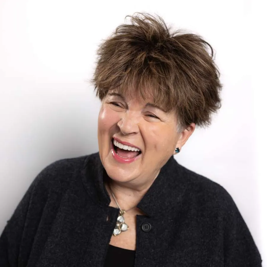 Middle-aged woman with short brown hair wearing black clothes laughing joyfully against white background