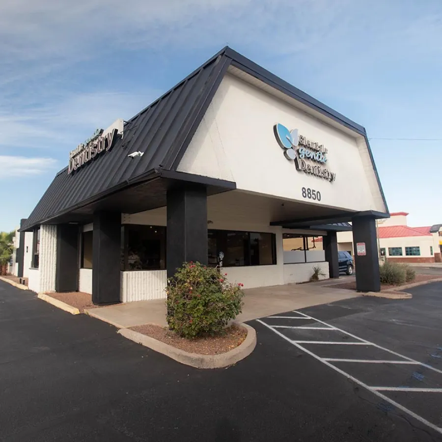 Exterior view of Glendale Gentle Dentistry building with black roof and parking area under a blue sky.