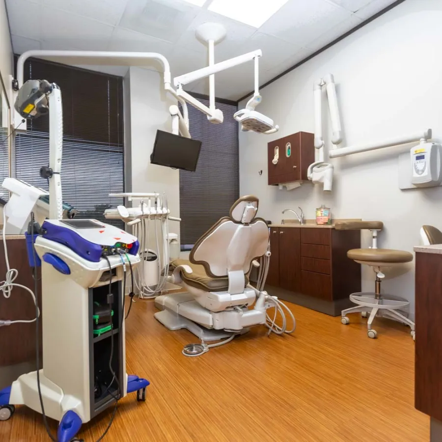 Modern dental clinic room with beige dental chair, equipment, monitor, and wood flooring under bright lights