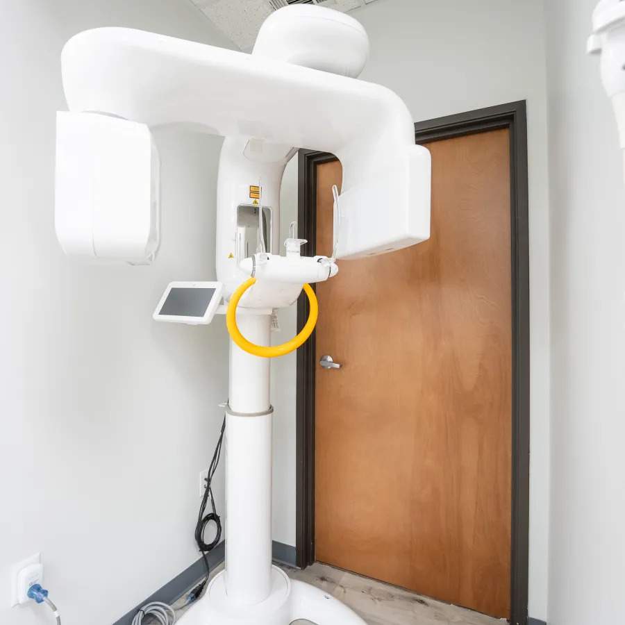 Modern dental panoramic X-ray machine with white walls and wooden door in imaging room.