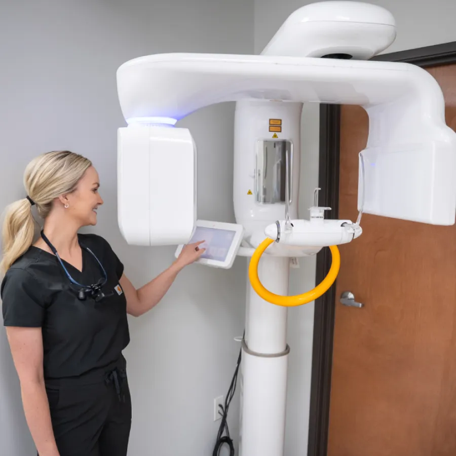 Dental professional operating a modern 3D panoramic X-ray machine in a clinic setting.