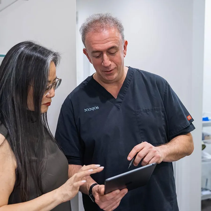 Doctor in medical scrubs explains tablet information to female patient in modern clinic setting.