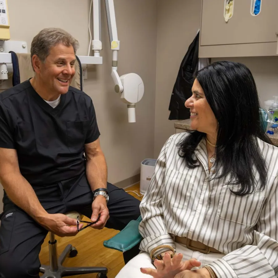 Dentist and patient smiling and discussing treatment in a modern dental office with equipment in background