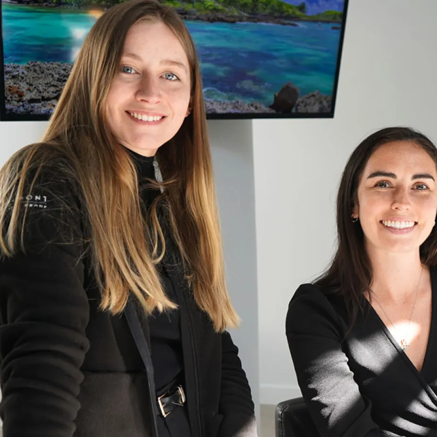 Three professional women smiling together in a modern office setting with a scenic backdrop.