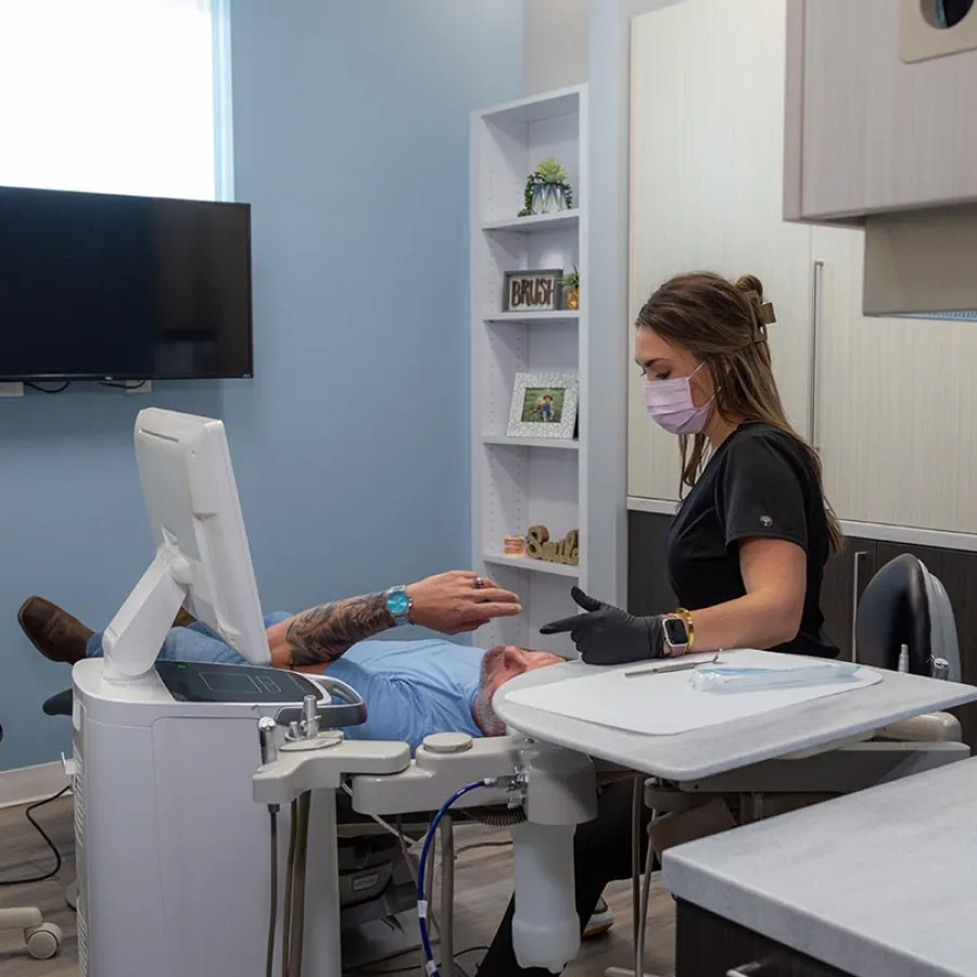 Dentist wearing mask and gloves consulting male patient reclining in dental chair in modern clinic room
