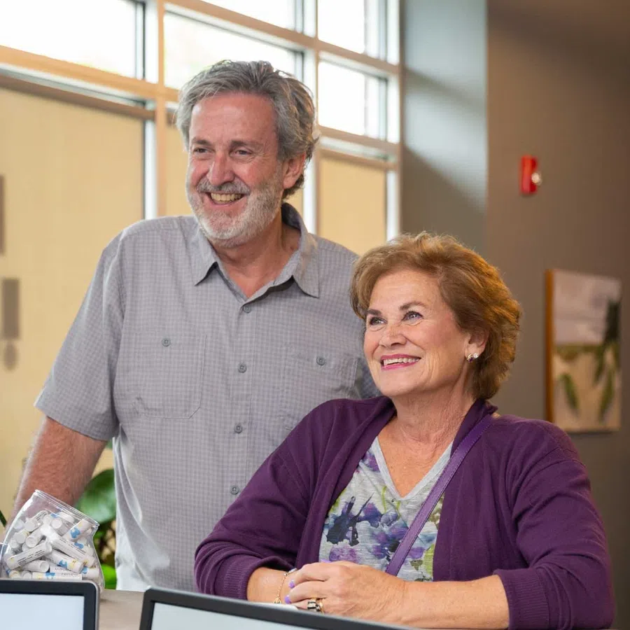 Smiling senior couple standing indoors near window, engaging happily in a bright modern room.