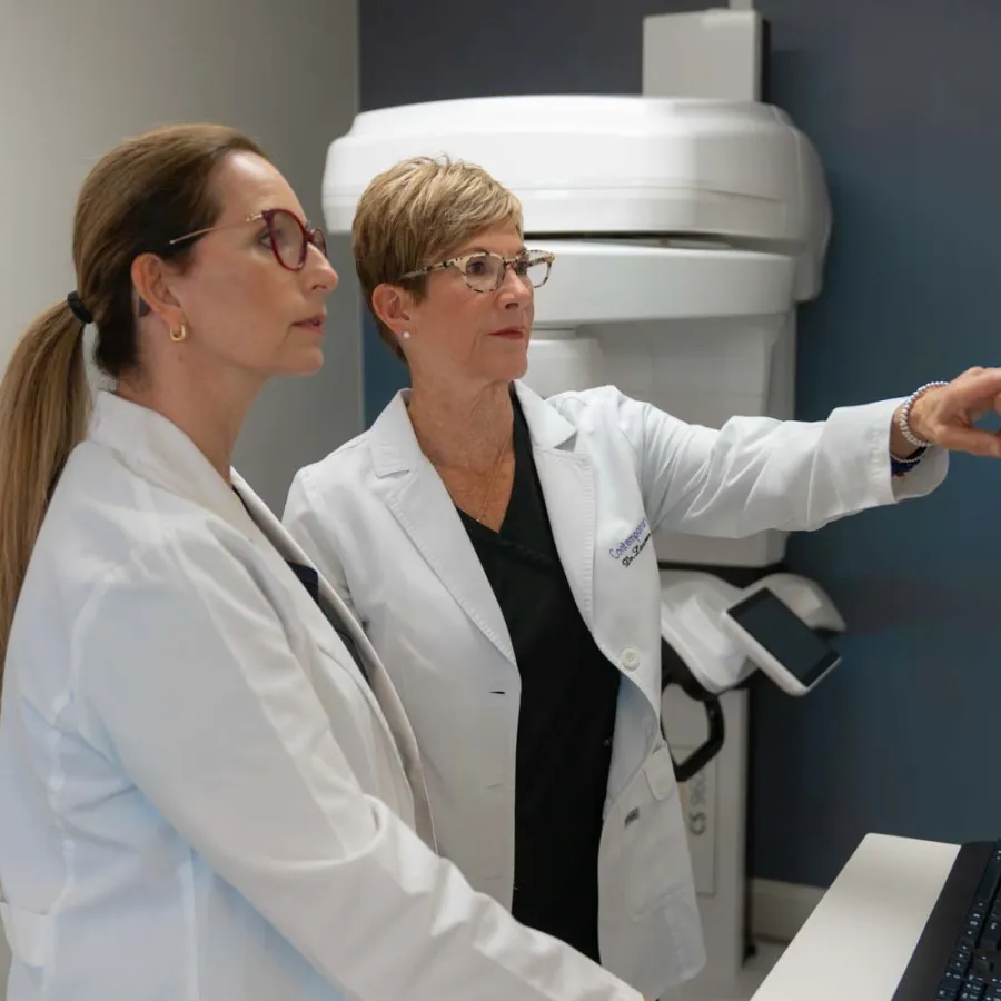 Two female doctors in white coats examining medical images on a computer screen in a clinic room.