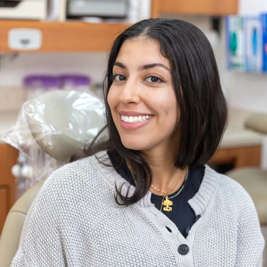 Smiling young woman sitting in a dental chair in a modern dental clinic setting looking at camera