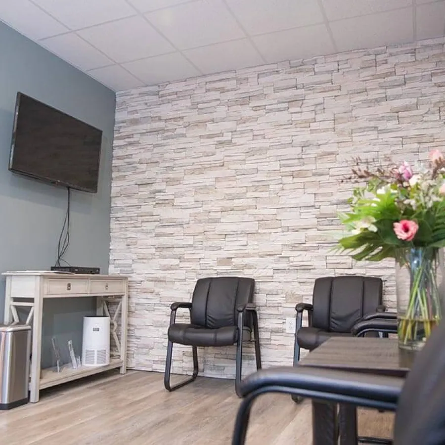 Modern waiting room with stone accent wall, black chairs, TV, white console table, and floral arrangement on table.