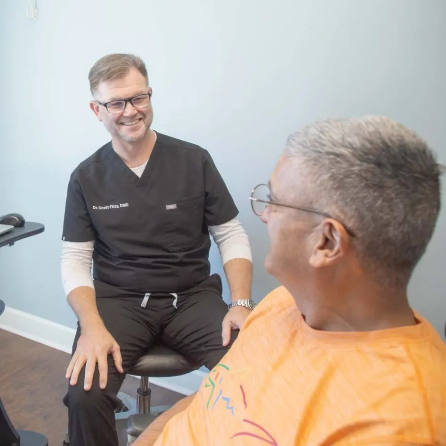 Dr. Scott Fitts in black scrubs smiles to a  patient