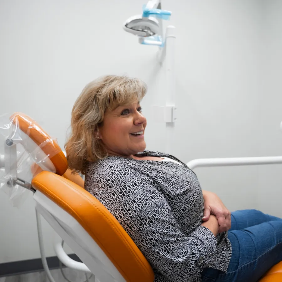 Middle-aged woman smiling while sitting in an orange dental chair inside a modern clinic room.