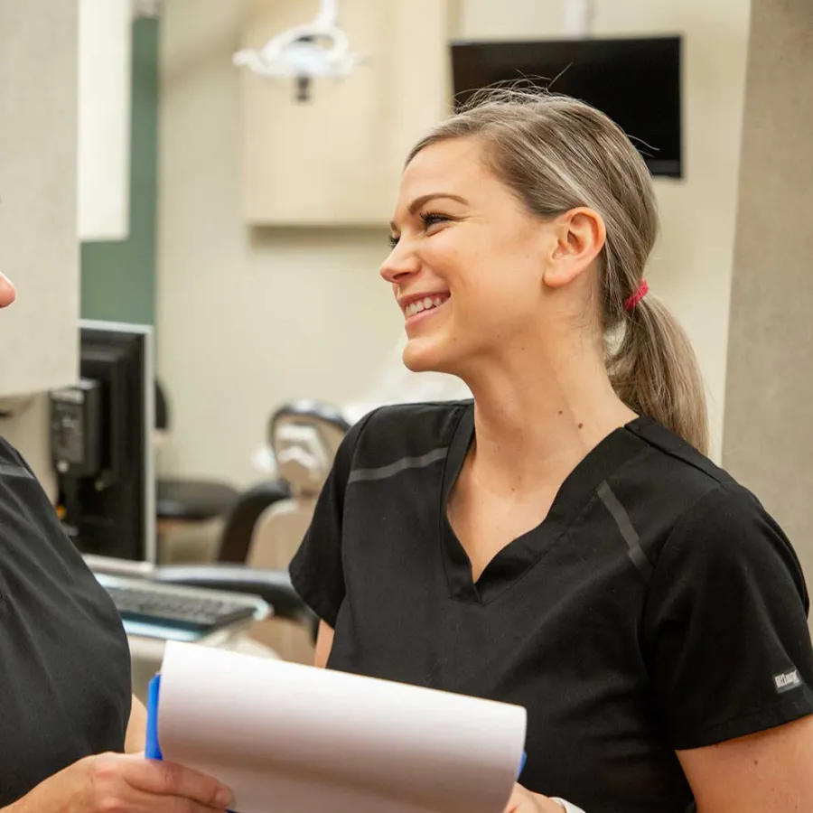 Two female healthcare professionals smiling and discussing notes in a medical office setting.