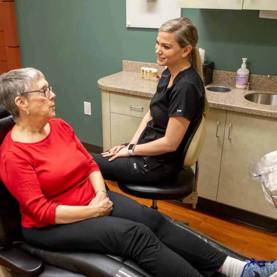 Senior woman in red shirt talking to female dental professional in clinic with modern equipment