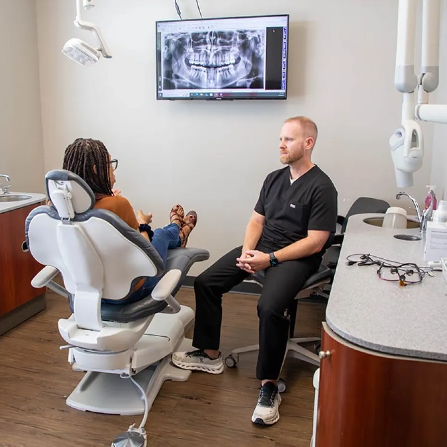Dentist consulting patient in dental office with dental X-ray displayed on screen.