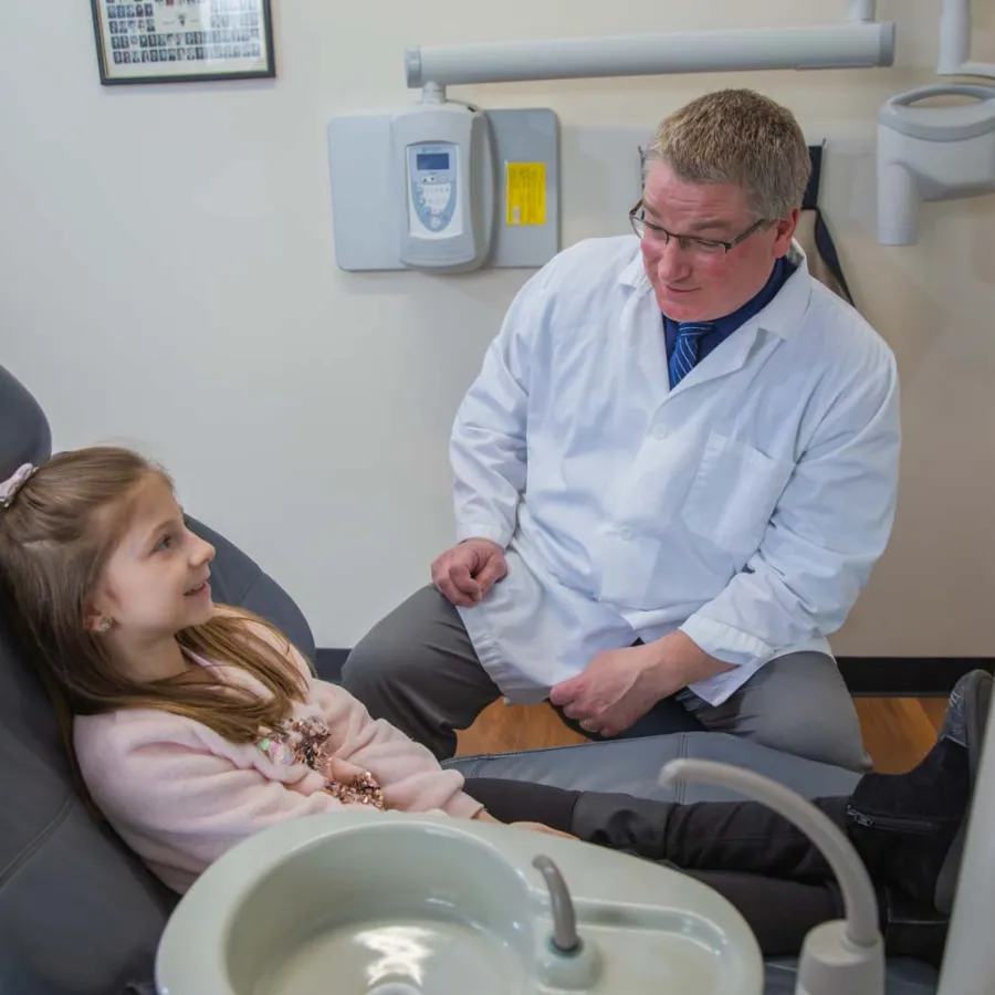 Dentist talking to young girl sitting in dental chair in a bright dental clinic room