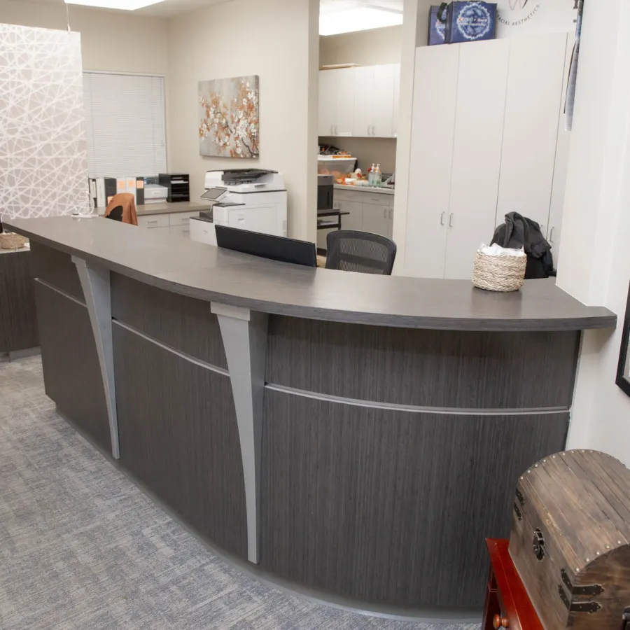 Modern curved reception desk in a clean office with bulletin board, clock, and storage cabinets