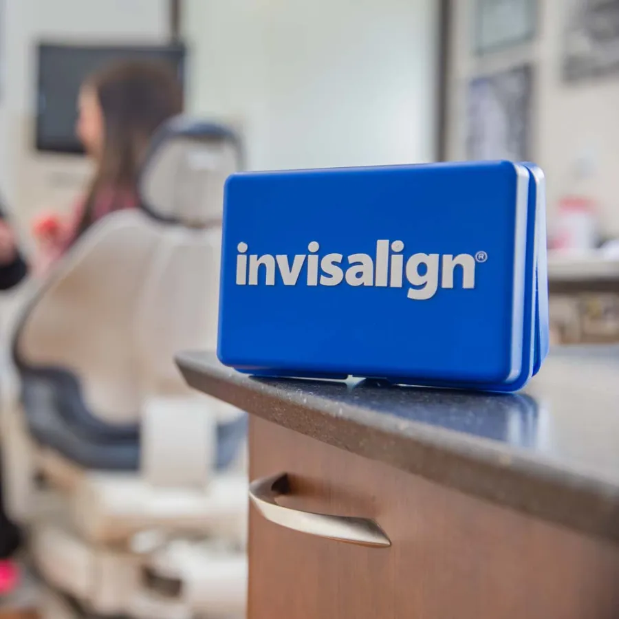 Blue Invisalign case on countertop in dental office with patient and dentist in blurred background.