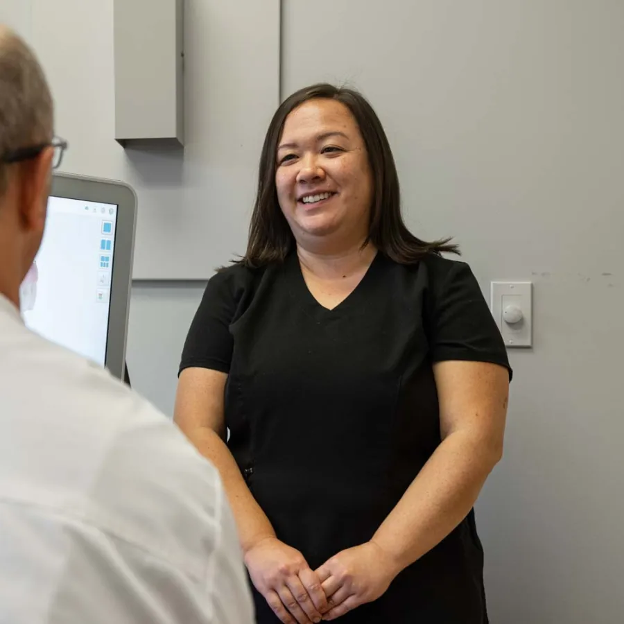 Smiling female healthcare professional talks with senior male patient in medical office with computer screen.