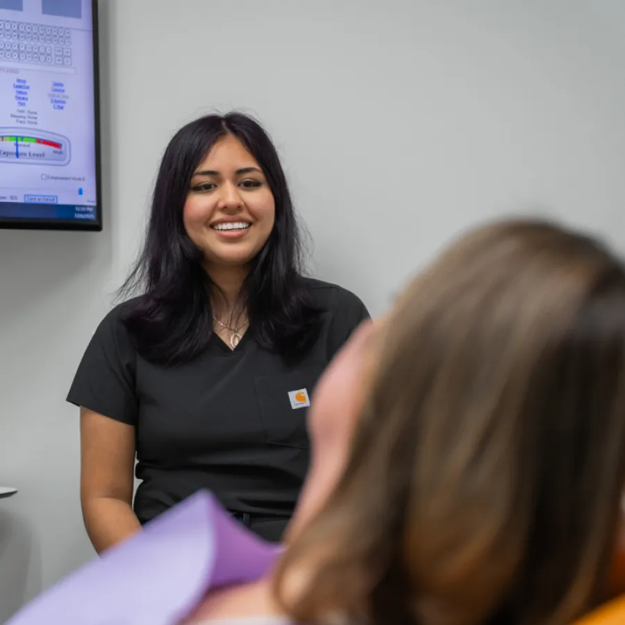 Smiling female healthcare professional talking to a patient in a clinical setting with medical monitor in background