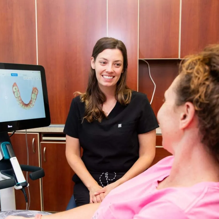 Dentist smiling and consulting with patient while dental 3D images display on computer screen in clinic.