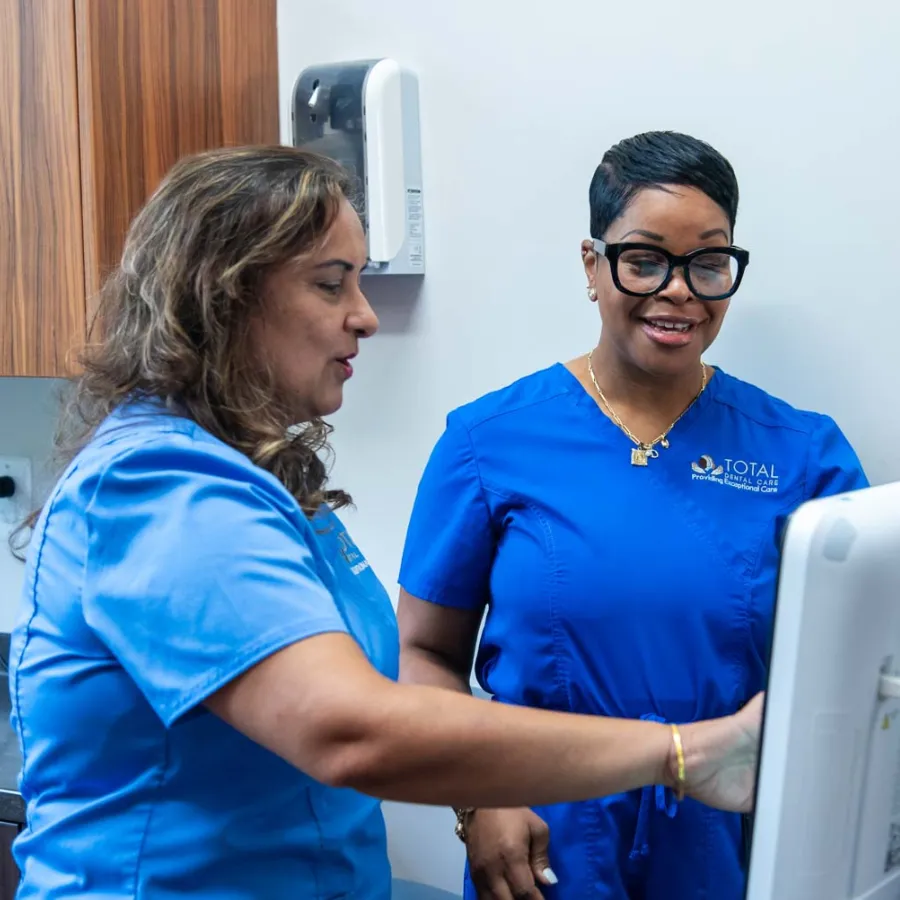 Two healthcare professionals in blue scrubs reviewing patient information on a computer in a clinical setting
