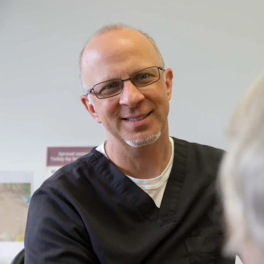 Smiling male healthcare professional in black scrubs talking to a patient with gray hair in a clinical setting.