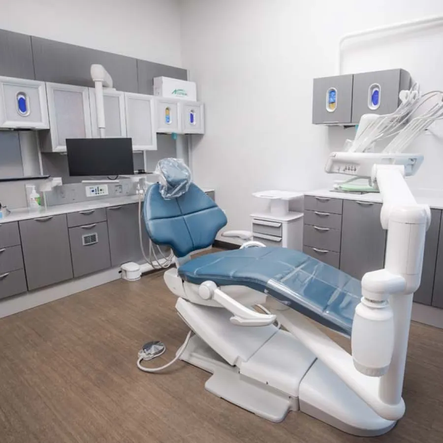 Modern dental office with blue dental chair, cabinetry, monitors, and dental equipment in clean treatment room