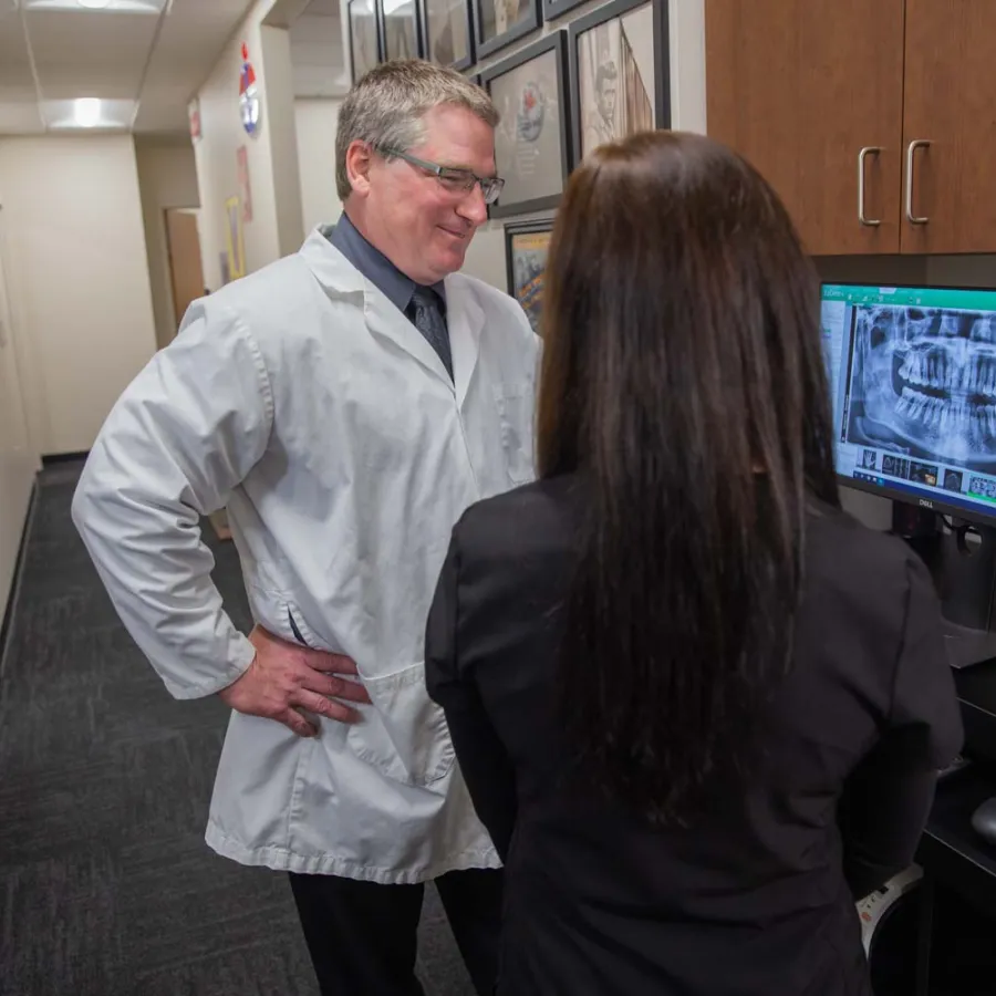 Dentist and patient reviewing a dental X-ray image on a computer screen in a clinic hallway.