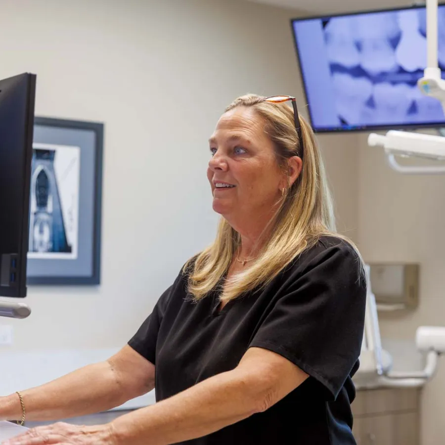 Female dental professional reviewing patient X-rays on computer screens in a modern dental office.
