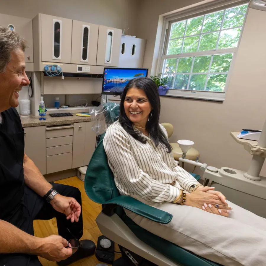 Dentist and female patient smiling and talking in a modern dental office with natural light.