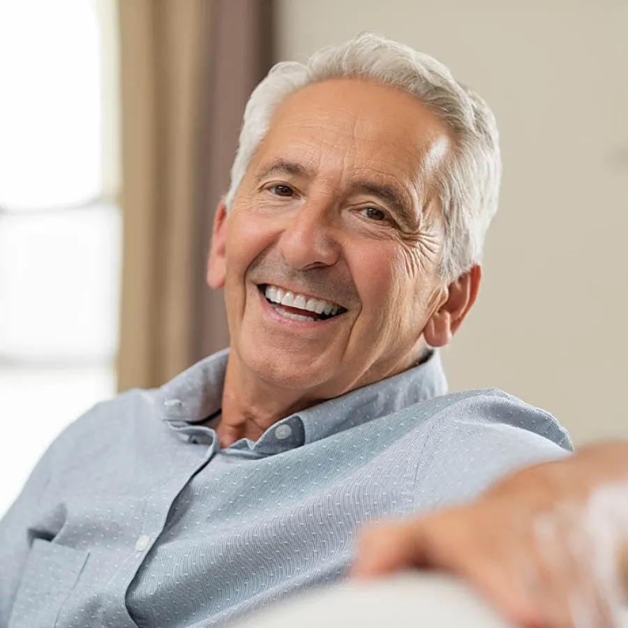 Smiling mature man with gray hair relaxing on a couch in a bright, comfortable room.