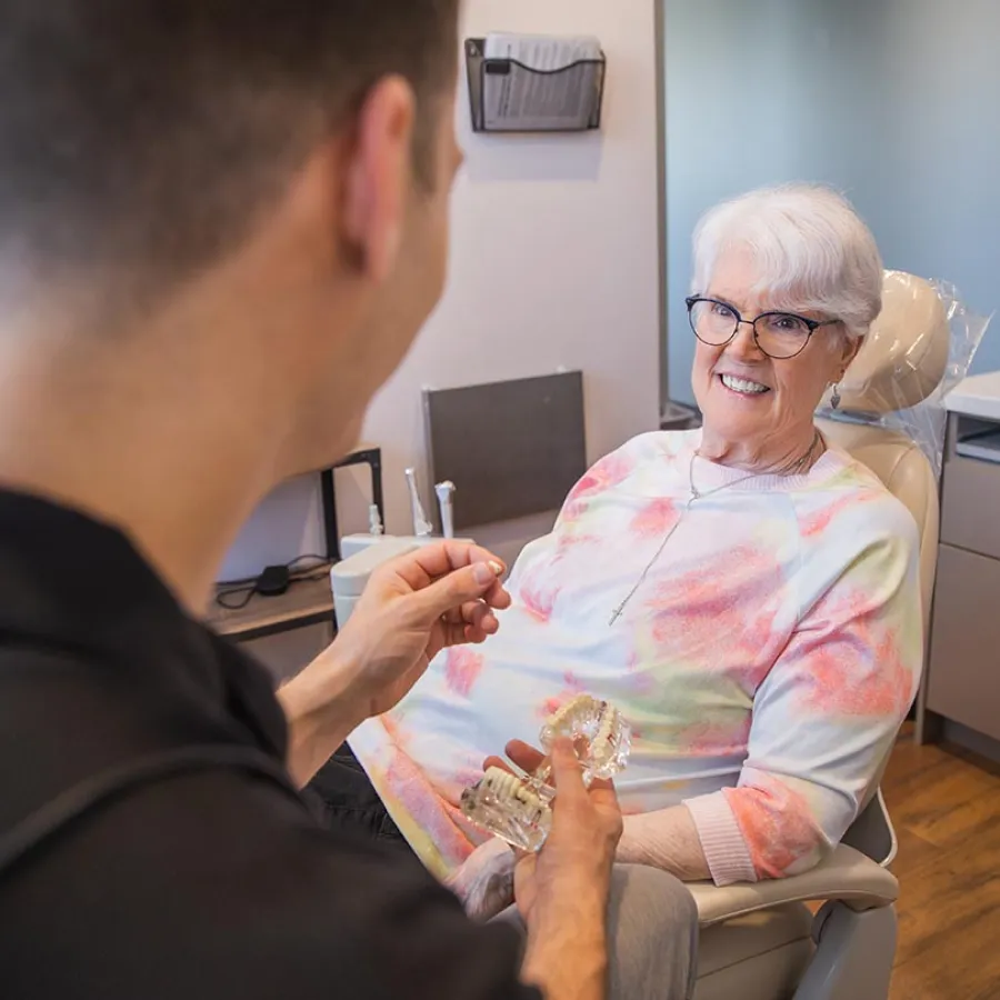 Dentist explaining dentures to elderly female patient in bright dental office with natural light.