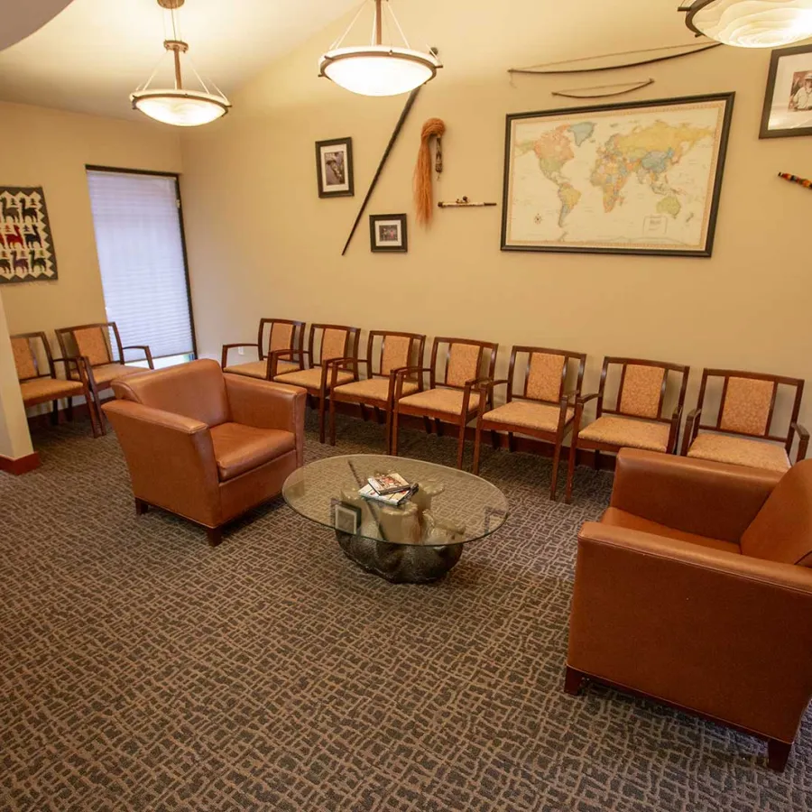 Waiting room with leather chairs, wooden seating, glass coffee table, and world map on the wall under warm lighting