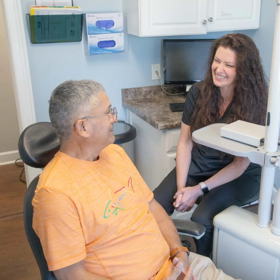 Dentist smiling and conversing with male patient in orange shirt at dental office during checkup.
