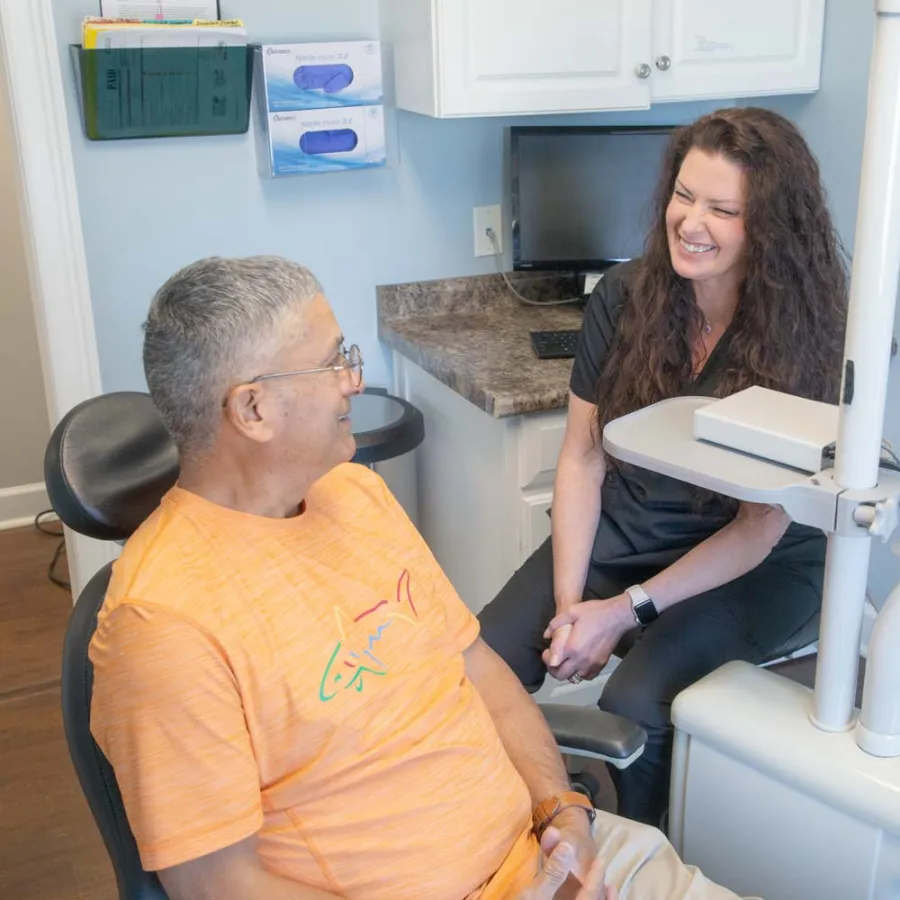 Dentist smiling and conversing with male patient in orange shirt at dental office during checkup.