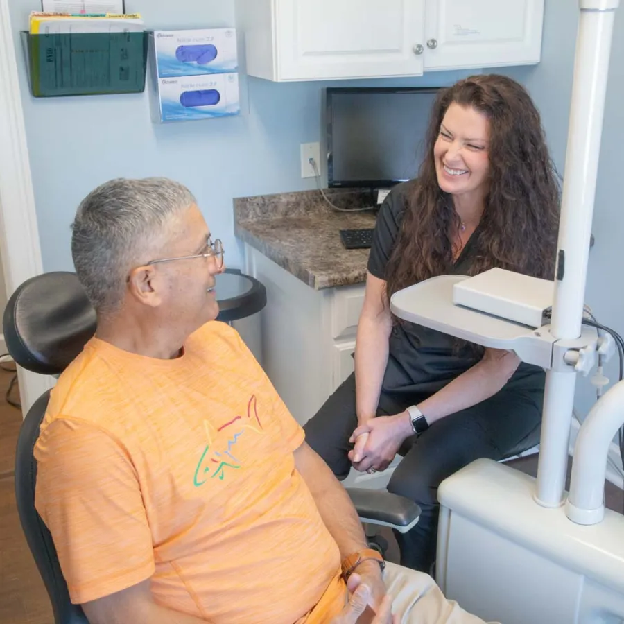 Dentist smiling and conversing with male patient in orange shirt at dental office during checkup.
