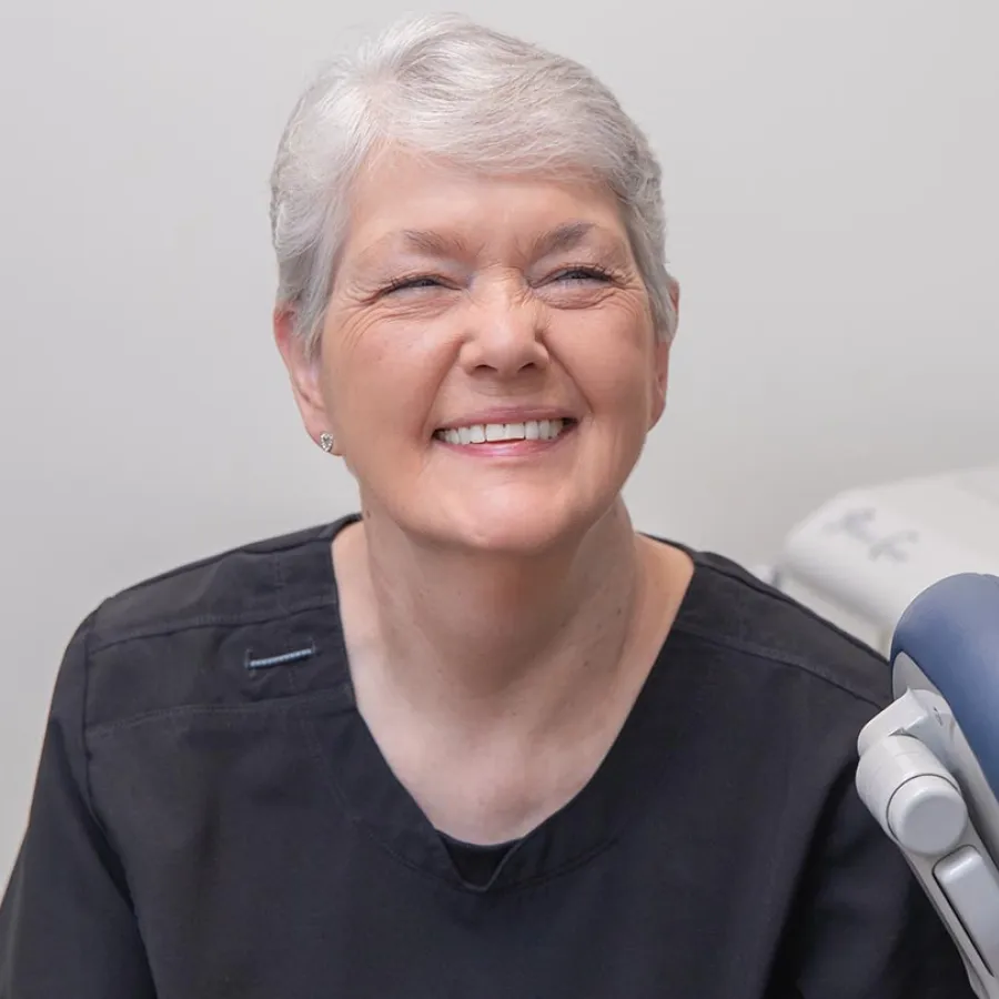 Smiling elderly woman with gray hair and black top in a medical or dental office setting.