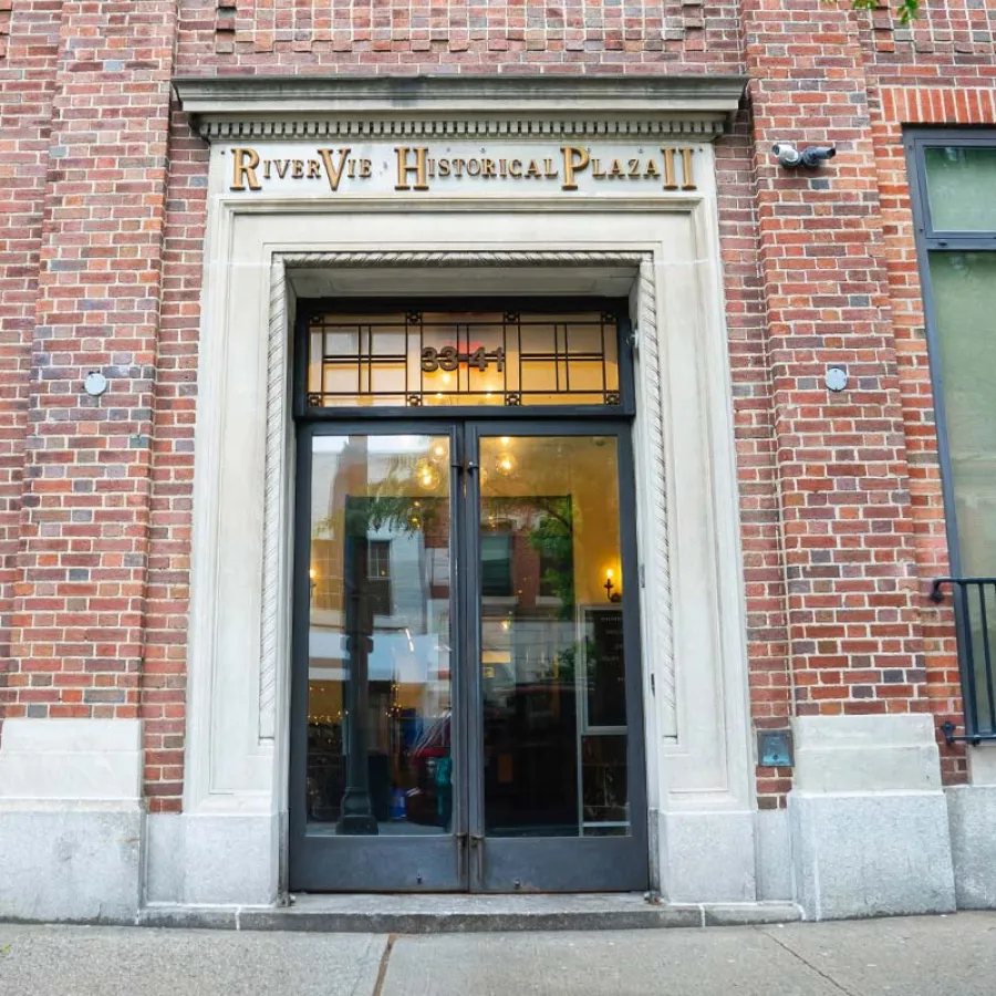 Entrance to River Vie Historical Plaza II with glass doors set in a brick building facade under decorative signage.