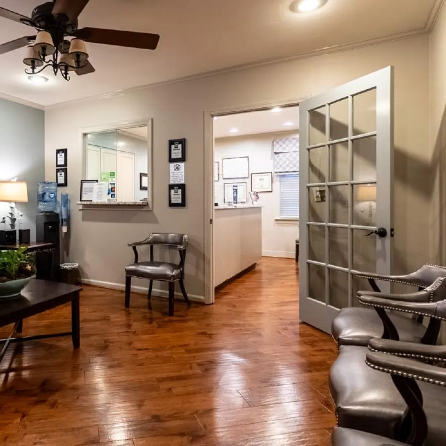 Comfortable waiting room with leather chairs, wooden flooring, ceiling fan, and open glass-paned door to reception area