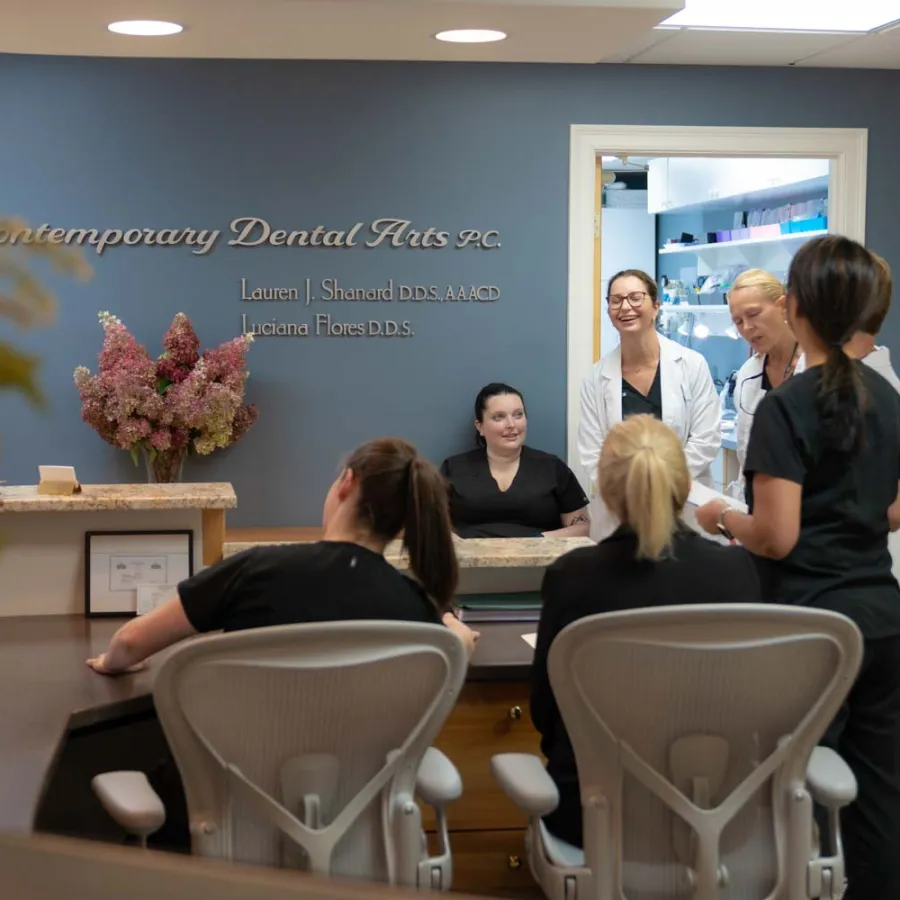 Dental clinic staff in scrubs and white coats chatting in a modern reception area with Contemporary Dental Arts sign.