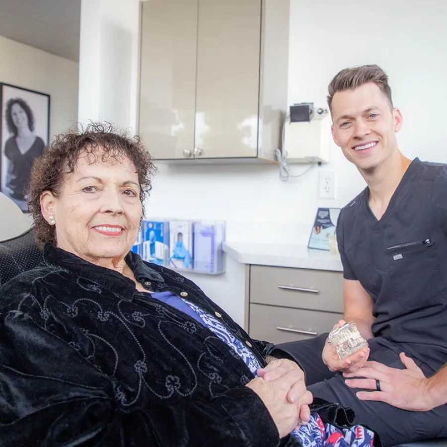 Senior woman smiling with a male dentist holding a dental model in a modern clinic setting.