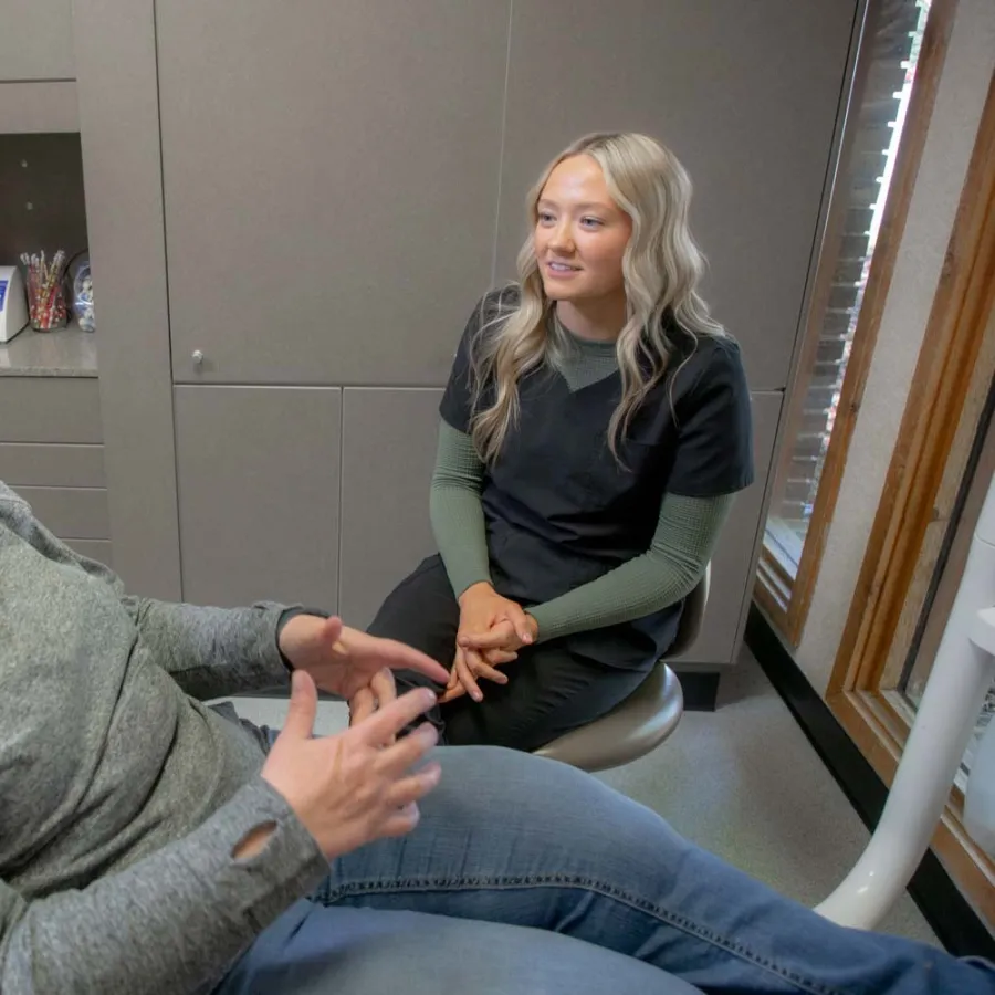 Woman patient talking with female dental professional in exam room during consultation.