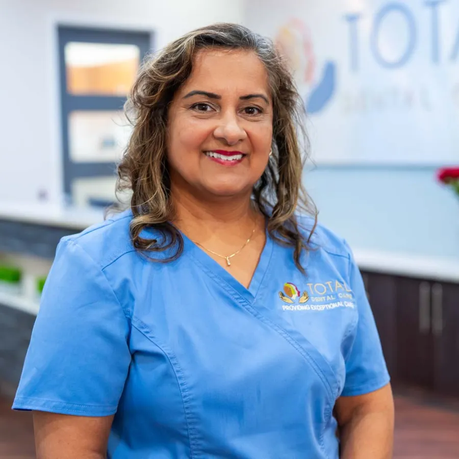 Smiling female dental professional in blue scrubs standing inside a modern dental clinic reception area.