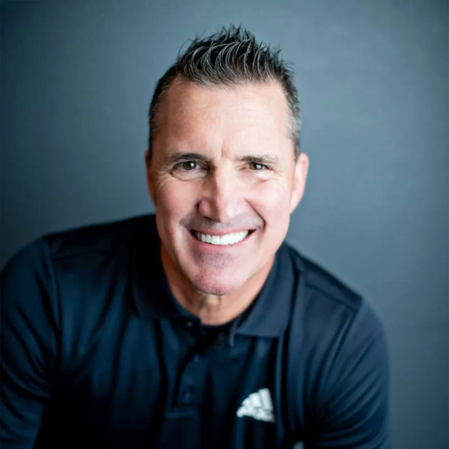 Smiling man in black Adidas polo shirt against plain gray background, close-up portrait with spiked hair.