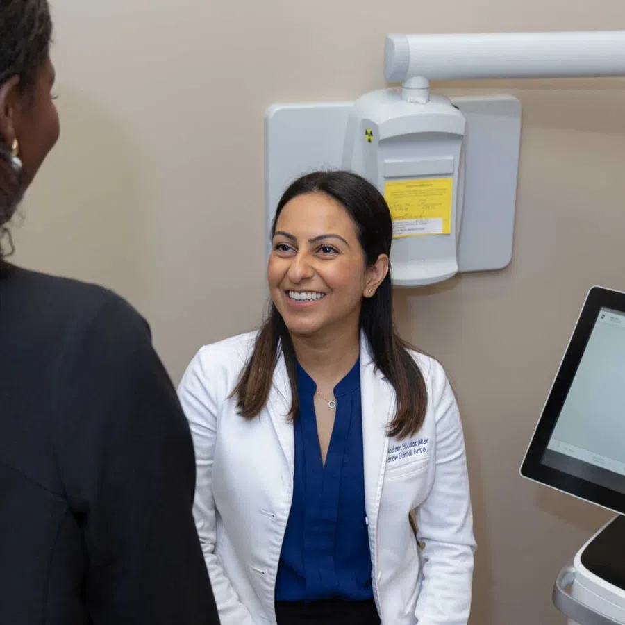 Dentist consulting with patient next to digital dental imaging equipment displaying teeth scan.