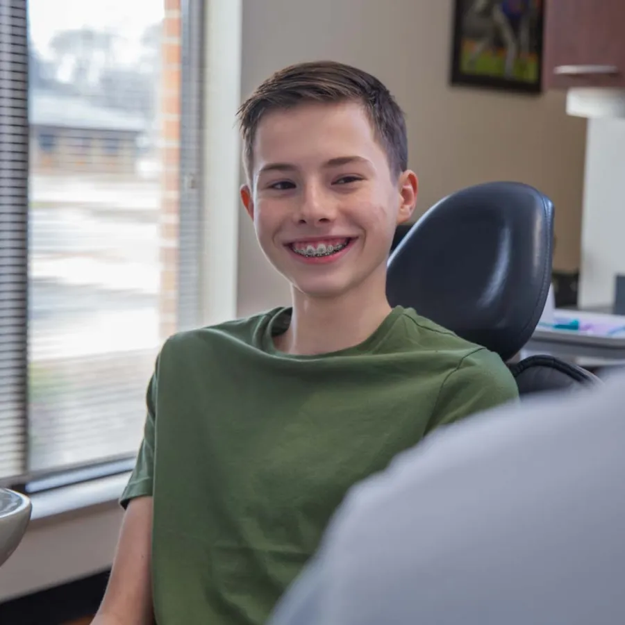 Smiling teenage boy with braces sitting in a dentist chair during a dental checkup in a modern clinic.