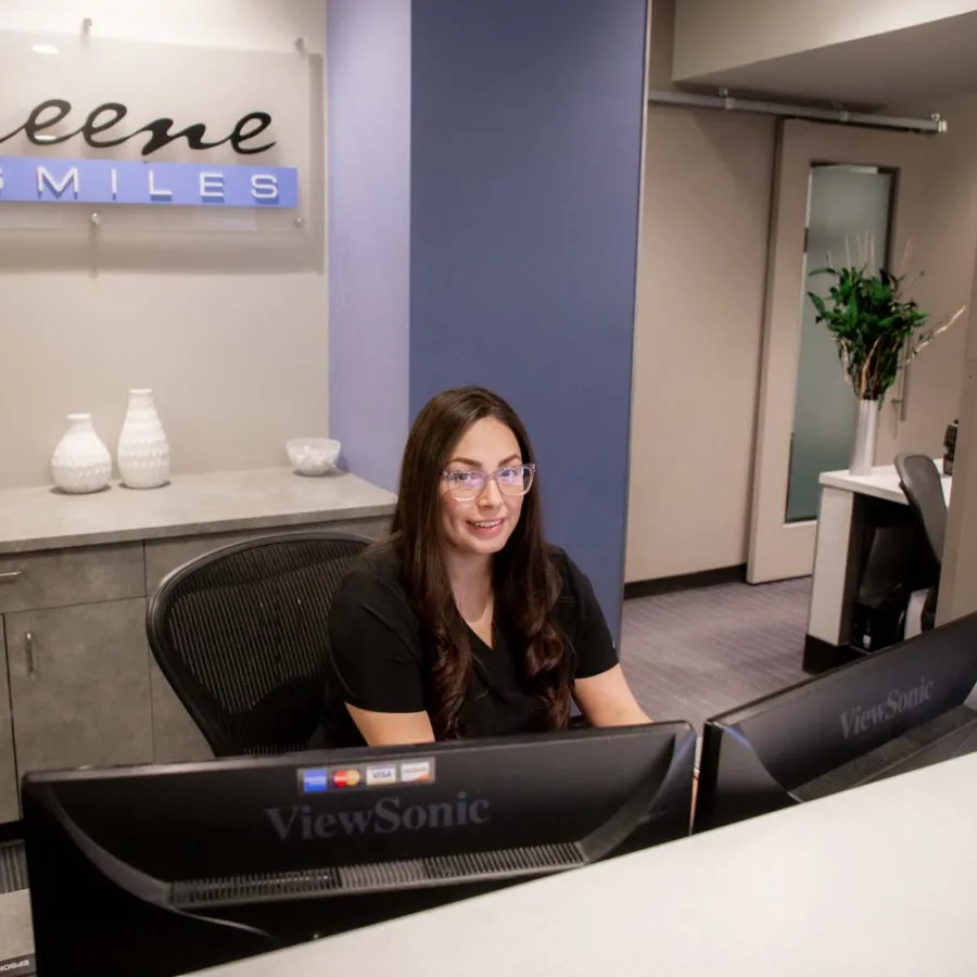 Receptionist smiling at Keene Smiles dental office behind dual ViewSonic monitors in a modern workspace
