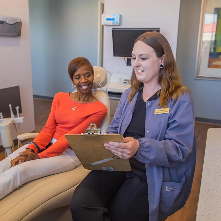 Two healthcare professionals in black scrubs smiling and discussing documents in a medical office.