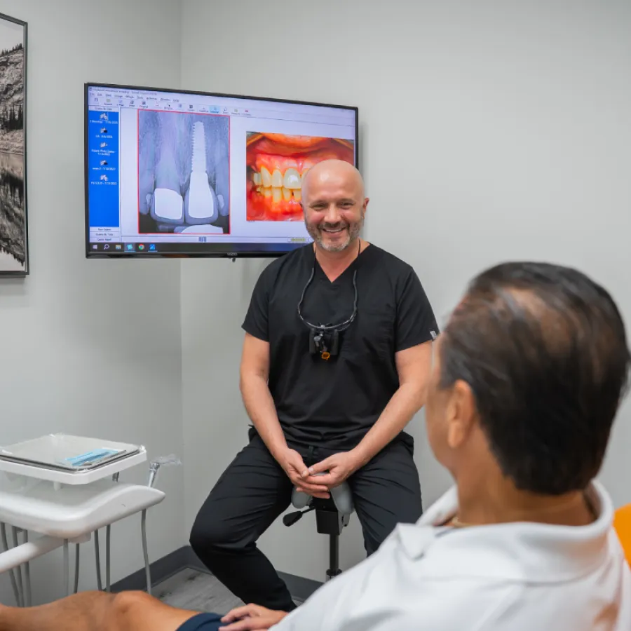 Dentist consulting patient with dental X-ray and teeth images displayed on screen in modern clinic
