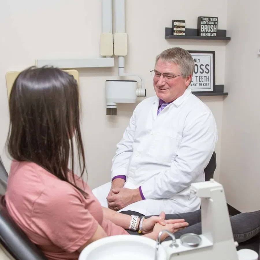 Dentist in white coat consulting female patient in dental office with dental equipment and health posters